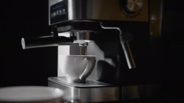 Kahve makinesinden fincana kahve dökülüyor. Ev yapımı sıcak Espresso. Filtre tutacağı kullanılıyor. Taze kahve akıyor. Sabahları kavrulmuş sade kahve içmek.