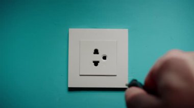 Adam mavi bir duvara elektrik prizi takıyor.