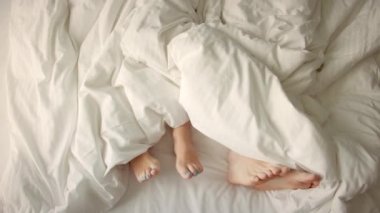 Çerçevede sadece bacaklar var. Aşık bir çift yatakta eğleniyor, ayaklarını farklı yönlere çeviriyor. Evlilik, aile, aşk. Evlilik, aile, aşk, seks konsepti. Sabah 4-K 'da..