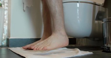 Bir adam tuvalete gelir, tuvalete oturur, külotunu çıkarır. Tuvaletteki bir adamın bacaklarına yakın çekim yap.
