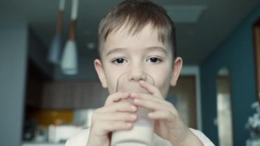 Küçük çocuk süt içiyor. Çocuk kahvaltısı yiyerek sağlıklı beslenme hayali. Kızım mutfakta yoğurt içiyor ve kefir dudaklarını yalıyor. pozitif çocuk kahvaltı yaparken gülümsüyor.