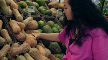 Genç bir kadın market alışverişi yapar, Hollowin tatili için süpermarketten balkabağı seçer. Pembe elbiseli çekici genç kadın sebze pazarından balkabağı sebzesi seçiyor.