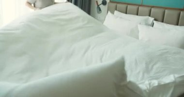 Genç, çalışkan, üniformalı kadın hizmetçiler beyaz çarşafları değiştirirken lüks otel odasını hazırlıyorlar..