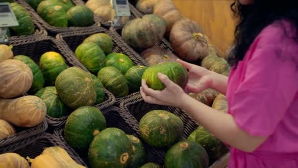 若い女性は食料品を買い スーパーでカボチャを選んでホロウィンの休日を過ごします ピンクのスーツを着た魅力的な若い女性が野菜市場でカボチャの野菜を選択します 女性の親密な関係 — ストック動画