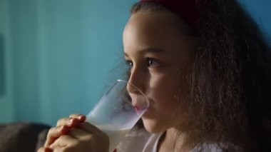 Küçük çocuk süt içiyor. Çocuk kahvaltısı yiyerek sağlıklı beslenme hayali. Kızım mutfakta yoğurt içiyor ve kefir dudaklarını yalıyor. pozitif çocuk kahvaltı yaparken gülümsüyor.