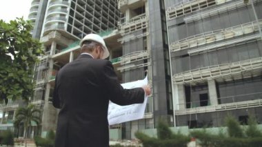 Güvenlik Üniforması ve Sert Şapka Giyen Profesyonel Kafkas Mühendis İşçi Portresi. Şema çizim planını kullanır. Kafkasyalı kendine güvenen endüstri uzmanı Fabrikada duruyor.