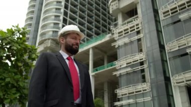 Sonuç olarak memnun olan mühendis kameraya gülümseyen, inşaat alanındaki tasarımcı inşaatın çok katlı binalarının sonuçlarını özetleyen bir başparmak gösteriyor.