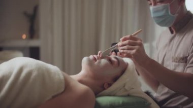Spa yatağında uzanıp yüz masajı yapan rahat bir kadın lüks spa merkezindeki masör, spa merkezinde yüz maskesi takan bir kız. Sağlık, stres atma ve gençleştirme kavramı.
