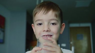 Küçük çocuk süt içiyor. Çocuk kahvaltısı yiyerek sağlıklı beslenme hayali. Kızım mutfakta yoğurt içiyor ve kefir dudaklarını yalıyor. pozitif çocuk kahvaltı yaparken gülümsüyor.