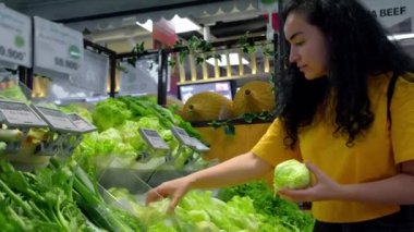 Pembe takım elbiseli çekici genç kadın lahana salatası seçiyor, süpermarketten alışveriş yapıyor, bakkaldan sağlıklı yiyecekler alıyor, marketten lahana salatası alıyor, süpermarketten. Market alışverişi kavramı