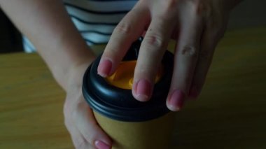 Parmaklarında pembe poz manikürlü bir kadının elleri bir kahve bardağıyla kağıt bardağı açar ve plastik kapağı açar. Tüm gün boyunca enerji artışı. Yavaş çekim 4K.