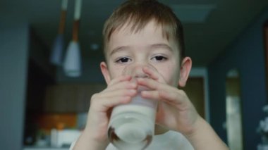 Küçük çocuk süt içiyor. Çocuk kahvaltısı yiyerek sağlıklı beslenme hayali. Kızım mutfakta yoğurt içiyor ve kefir dudaklarını yalıyor. pozitif çocuk kahvaltı yaparken gülümsüyor.