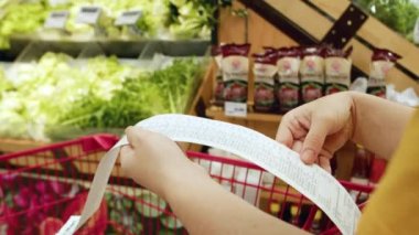 Alışveriş merkezinden alışveriş yaptıktan sonra alışveriş arabasındaki Sevgili Miktar faturasını kontrol eden bir kadın. Gıda fiyatlarında artış, hipermarkette para harcamak