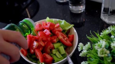 Kadın eli, metal bir kâseye zeytinyağı ekliyor sebze salatasıyla, yavaş çekimde..