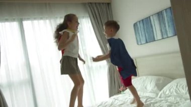 Kız ve erkek süper kahramanlar, yatakta, çocuk odasında, kırmızı ve mavi Süpermen kostümlü iki çocuk, süper kahramanlar, erkek ve kız kardeşler, kendilerini süper kahraman olarak hayal ederek oynuyorlar..