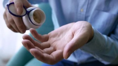 Yaşlı yetişkin bir adam, elinde erkek eline ağrı kesici hapları tutarak ilaç şişesinden iki kapsül dolduruyor, yaşlı büyükanne sağlık hizmetleri, eczane ve tedavi konsepti, yakın görüş..