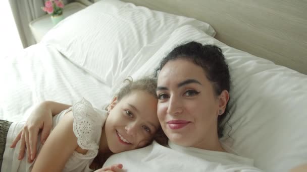 ベッドルームで寝そべっている間に母と娘の肖像画が電話で自撮り ママと娘はカメラと笑顔を見て 母親という概念は — ストック動画