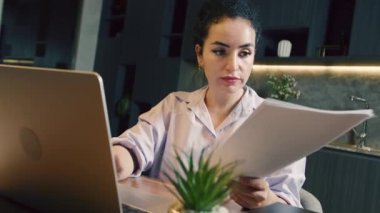 Laptop klavyesinde daktilo eden Kafkasyalı genç bir iş kadını ev ofisinde oturuyor. Laptop bilgisayarına bakan etnik iş kadını, vergi belgelerinin uzlaşması, evdeki uzaktan çalışma.