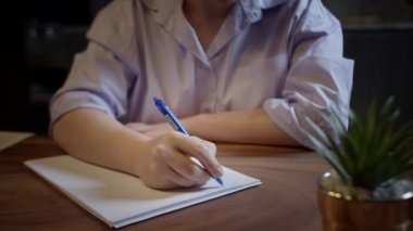 Masasında oturan beyaz bir kadın elinde kalemle günlüğe not alıyor, manzarayı kapatıyor. İş kadını yeni başlayan iş fikirleri ve planlar yazar. Not defterine yaratıcı düşünceler yazar. Yapılacaklar ya da istekler listesi oluştur