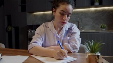 Masasında oturan beyaz bir kadın elinde kalemle günlüğe not alıyor, manzarayı kapatıyor. İş kadını yeni başlayan iş fikirleri ve planlar yazar. Not defterine yaratıcı düşünceler yazar. Yapılacaklar ya da istekler listesi oluştur