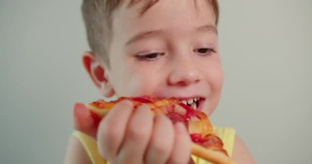 肖像画の子供を閉じます幸せな面白い小さな男の子が熱心においしいピザを食べ 笑顔の子供が自宅でイタリアのピザを食べてカメラを見て かわいい子供が熱心に直面しています コンセプト幸せな子供時代 — ストック動画