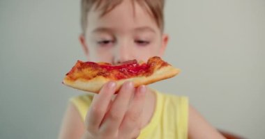 Portre Çocuk 'u yakın çekim mutlu küçük çocuk hevesle lezzetli pizzalar yiyor, evde kameraya bakıp İtalyan pizzası yiyen gülümseyen çocuk, güzel yüzlü şirin çocuk. Mutlu çocukluk kavramı