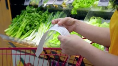 Alışveriş merkezinden alışveriş yaptıktan sonra alışveriş arabasındaki Sevgili Miktar faturasını kontrol eden bir kadın. Gıda fiyatlarında artış, hipermarkette para harcamak