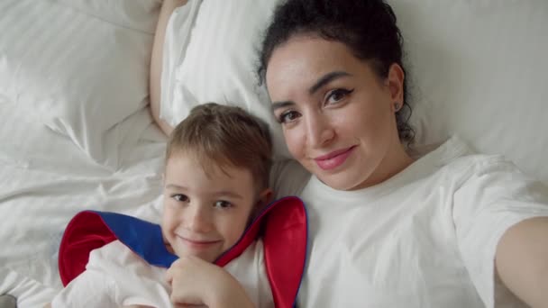 肖像快乐可爱有趣快乐的妈妈和儿子轻轻地拥抱 儿子和妈妈在床上躺在卧室里用手机自拍 妈妈和儿子看着相机 母亲的概念 — 图库视频影像