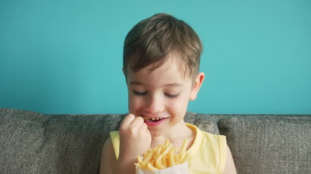 子供は青い背景でフライドポテトを食べる かわいい女の子はポテトフライを食べる彼女の指をなめる 空腹の赤ん坊はファーストフードを食べる 小さな女の子が喜んで揚げライフスタイルジャガイモを食べる — ストック動画