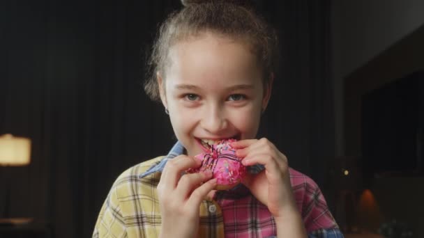 Caucasian子10歳は釉薬で食欲をそそる甘いデザートを食べます 陽気な少女は甘いドーナツを食べる 子供の口の近くに甘いペストリーを食べている — ストック動画