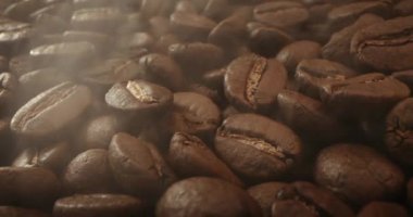 Makro fırında kahve çekirdeği vurdu. Aromatik kahve çekirdekleri kahve çekirdeklerinin kızartılışından çıkan koyu renkli dumanların içinde yavaşça hareket eder. Kavrulmuş kahve çekirdeklerini dumanla yakın plan çek.