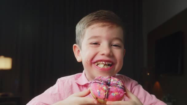 Caucasian子6歳は釉薬で食欲をそそる甘いデザートを食べます 陽気な少年は甘いドーナツを食べる 子供の口の近くに甘いペストリーを食べている — ストック動画