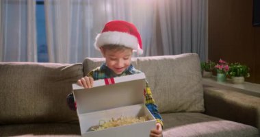 Mutlu şirin çocuk, sürprizden zevk alır, bir Noel hediyesi kutusunu açar ve hediyesinden aldığı mutlulukla yere düşer. Portre güzel küçük çocuk, çocuk Noel sürprizi ile kutuyu açıyor..