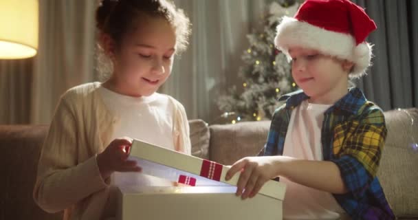 驚きに満ちた幸せなかわいい子供たちは ボックスクリスマスギフトを開き 彼の贈り物から喜びで幸せに落ちます 肖像画の美しい小さな男の子 子供はクリスマスの驚きで箱を開きます — ストック動画