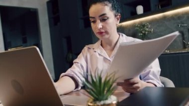 Laptop klavyesinde daktilo eden Kafkasyalı genç bir iş kadını ev ofisinde oturuyor. Laptop bilgisayarına bakan etnik iş kadını, vergi belgelerinin uzlaşması, evdeki uzaktan çalışma.