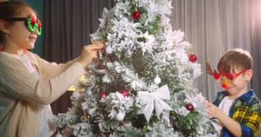 Çocuklar elinde Noel ağacı için çok güzel bir Noel balosu tutuyor. Mutlu çocuklar Noel ağacını toplarla süslerler. Ağacın altında bir sürü hediye kutusu var. Çocuk Noel ağacını süslüyor