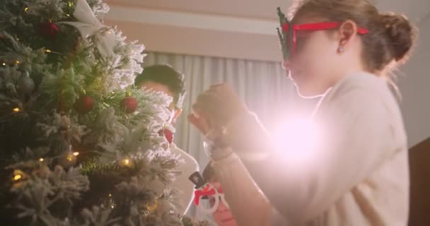 幸せな子供たちはボールでクリスマスツリーを飾ります 木の下にたくさんのギフトボックス 子供たちは彼の手でクリスマスツリーのための美しい装飾クリスマスボールを保持しています — ストック動画
