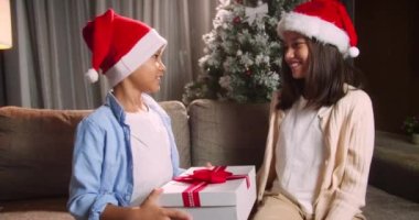 Mutlu şirin çocuklar sürprizle şenlenir, çocuklar Noel hediyelerini verir, kız hediyesini alır ve hediye kutusunu açar. Noel Baba şapkalı mutlu çocuklar portresi.