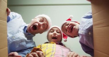 Mutlu baba ve çocukları, sürprizden çok memnun kalarak, hediyelerle dolu bir kutu açtılar. Küçük çocuklar, bir kız ve bir erkek kardeş, karton bir kutuya bakın. İçeriden. Çocuklar ellerini kutunun içine sokuyor..