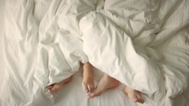 Çerçevede sadece bacaklar var. Aşık bir çift yatakta eğleniyor, ayaklarını farklı yönlere çeviriyor. Evlilik, aile, aşk. Evlilik, aile, aşk, seks konsepti. Sabah 4-K 'da..