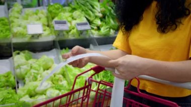 Alışveriş merkezinden alışveriş yaptıktan sonra alışveriş arabasındaki Sevgili Miktar faturasını kontrol eden bir kadın. Gıda fiyatlarında artış, hipermarkette para harcamak