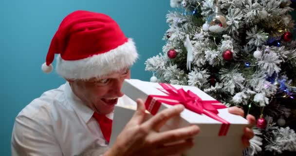 クリスマスの帽子のハッピーマンお父さんサンタ クラウザは彼の妻と子供 お父さん 男からサプライズボックスで贈り物を受け取り サプライズに喜んで 贈り物で箱を開けます — ストック動画