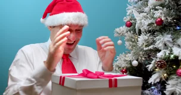 クリスマスの帽子の幸せなお父さんサンタクロースは贈り物を受け取り 驚きで箱を見て お父さんは顔を驚かせ 失望した人の顔 悪い驚き 男は不快な何かで小包ボックスを開く — ストック動画