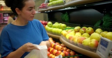 Kadın olgun armutları raftan alır ve bir sepete koyar. Çekici genç kadın marketten taze armut sebzesi seçiyor. Market kavramı.