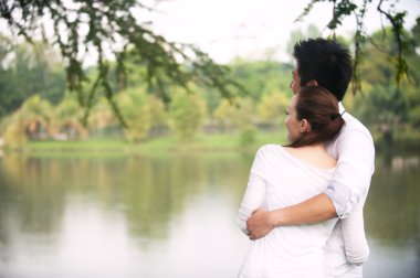 Parkta kucaklaşan Asyalı çift.