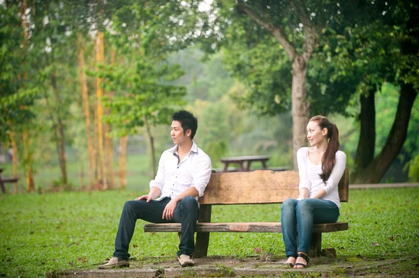 Asiática joven pareja sentado fuera al aire libre en un banco — Foto de Stock