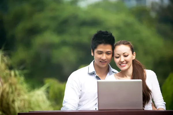 Asiático casal sentado em um parque e olhando para laptop — Fotografia de Stock