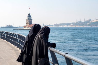Geleneksel Müslüman kıyafetli iki kadın siyah tesettür, çarşaf giyiyor ve İstanbul, Türkiye 'de toprak setinde yürüyor
