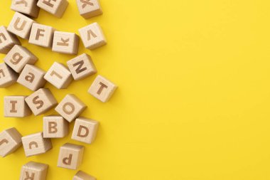Yüzeyinde harfler olan ahşap eğitim küpleri sarı arka planda yatıyor