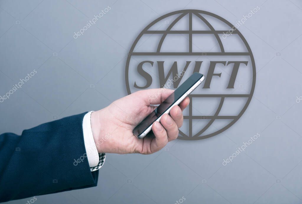 MOSCOW - MARCH 04: A man businessman dressed in suit holding smartphone in front of SWIFT logotype on a wall in Moscow, March 04. 2022 in Russia